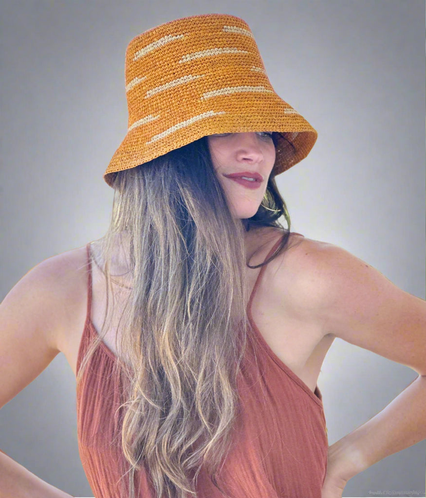 Model wearing 2.5" Brim Taylor Saffron Crochet Bucket Straw Hat with Zebra Stripes handmade raffia palm fiber in a two tone color combination of horizontal short stripes that create a dash pattern around the hat in saffron yellow/orange with natural straw color - Shebobo