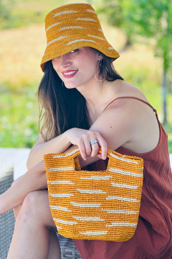 Model wearing Taylor Mini ConCon Crochet Saffron Straw Basket with Zebra Stripes handmade raffia palm fiber in a horizontal zebra stripe with short lengths of contrasting color in a dash pattern of saffron yellow/orange with natural straw color accent petite handbag purse with matching 2.5" Brim Taylor Crochet Bucket Straw Hat  - Shebobo