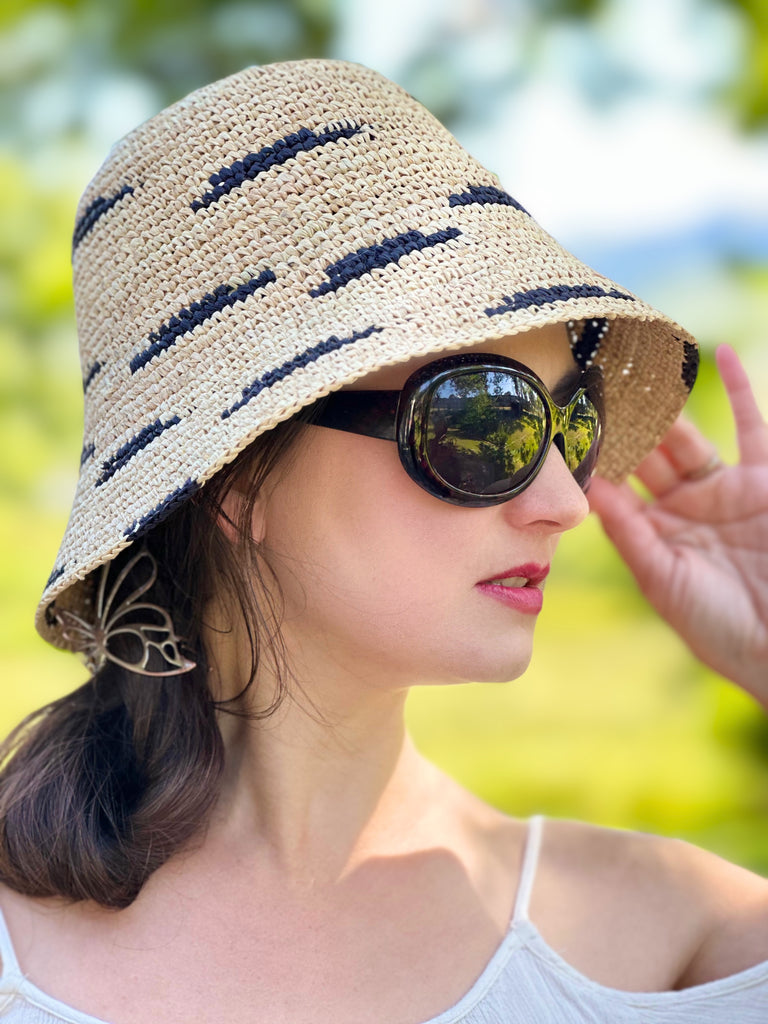 Model wearing 2.5" Brim Taylor Natural Crochet Bucket Straw Hat with Zebra Stripes handmade raffia palm fiber in a two tone color combination of horizontal short stripes that create a dash pattern around the hat in natural straw color with black - Shebobo