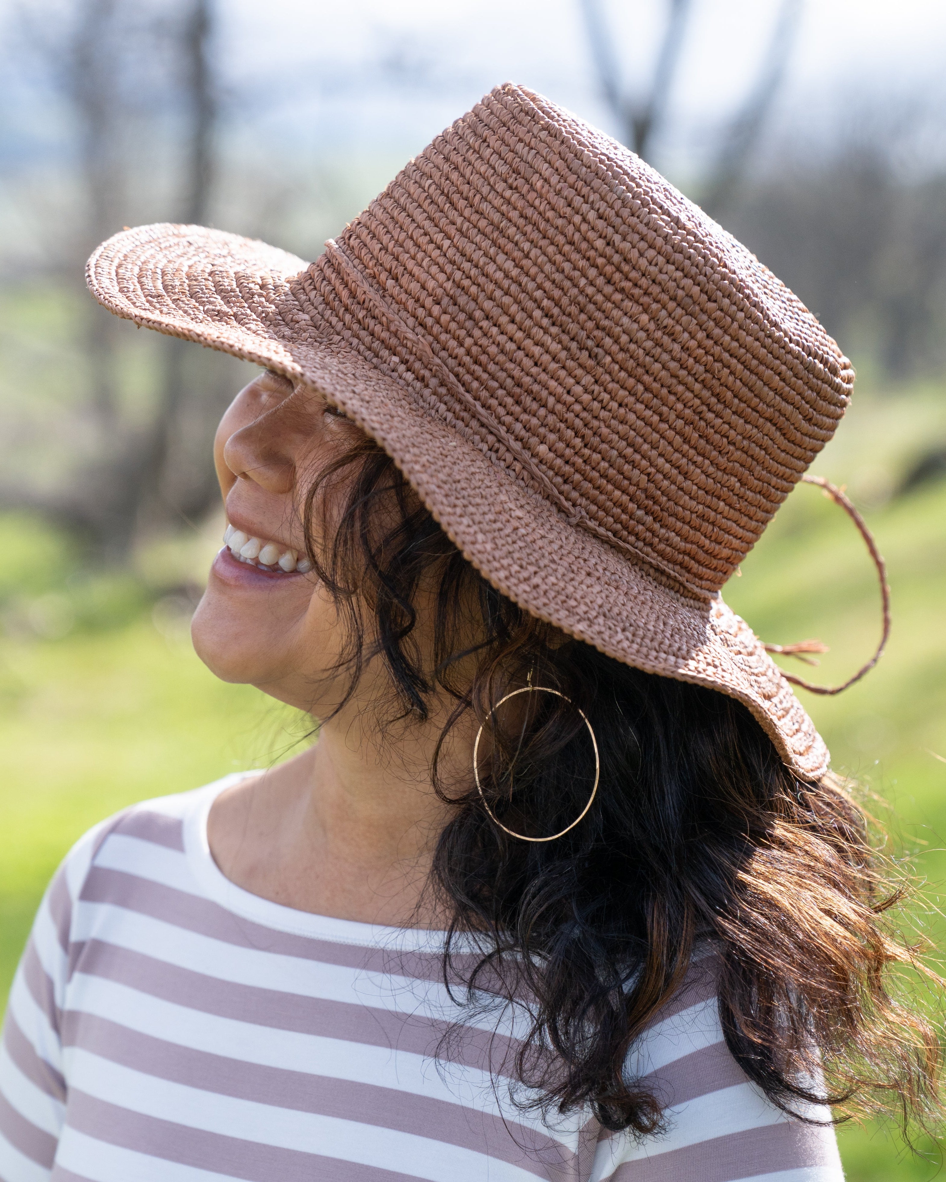 Model wearing 3" Brim Bolero Crochet Straw Sun Hats handmade crochet natural raffia palm fiber in a solid hue of cinnamon dark brown making a concentric pattern from the center top of the flattened crown spiraling out to the edge of the brim with matching adjustable raffia braid hat band - Shebobo
