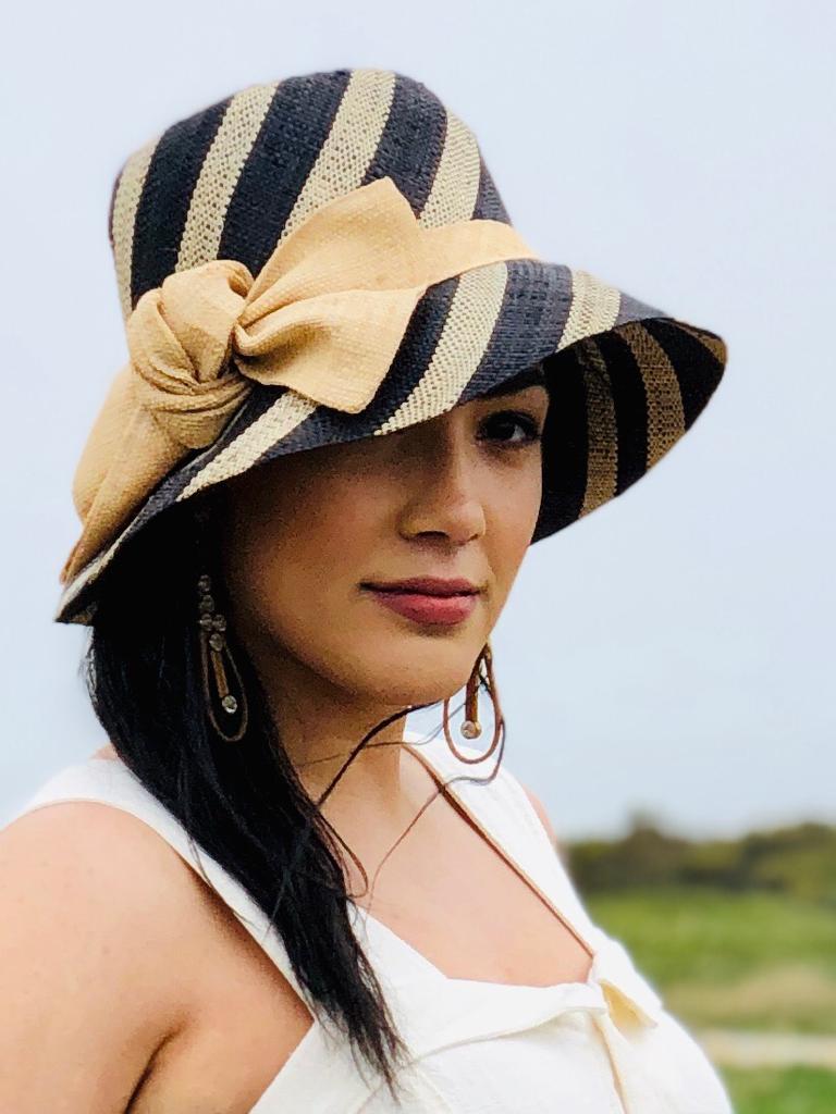 Model wearing 3 inch brim Cara Straw Hat with Big Bow handmade loomed raffia in bands of black and natural straw color stripes that create a swirl pattern on the crown and brim with a natural color hat band and extra large bow embellishment - Shebobo
