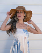 Model wearing 5.5" Brim Gigi Cinnamon and Natural Floral Embroidered Crochet Straw Sun Hats handmade crochet natural raffia palm fiber in a solid hue of cinnamon dark brown making a concentric pattern from the center top of the flattened crown spiraling out to the edge of the brim with matching adjustable raffia braid hat band and natural straw color floral pattern with leaves embroidered on the brim - Shebobo