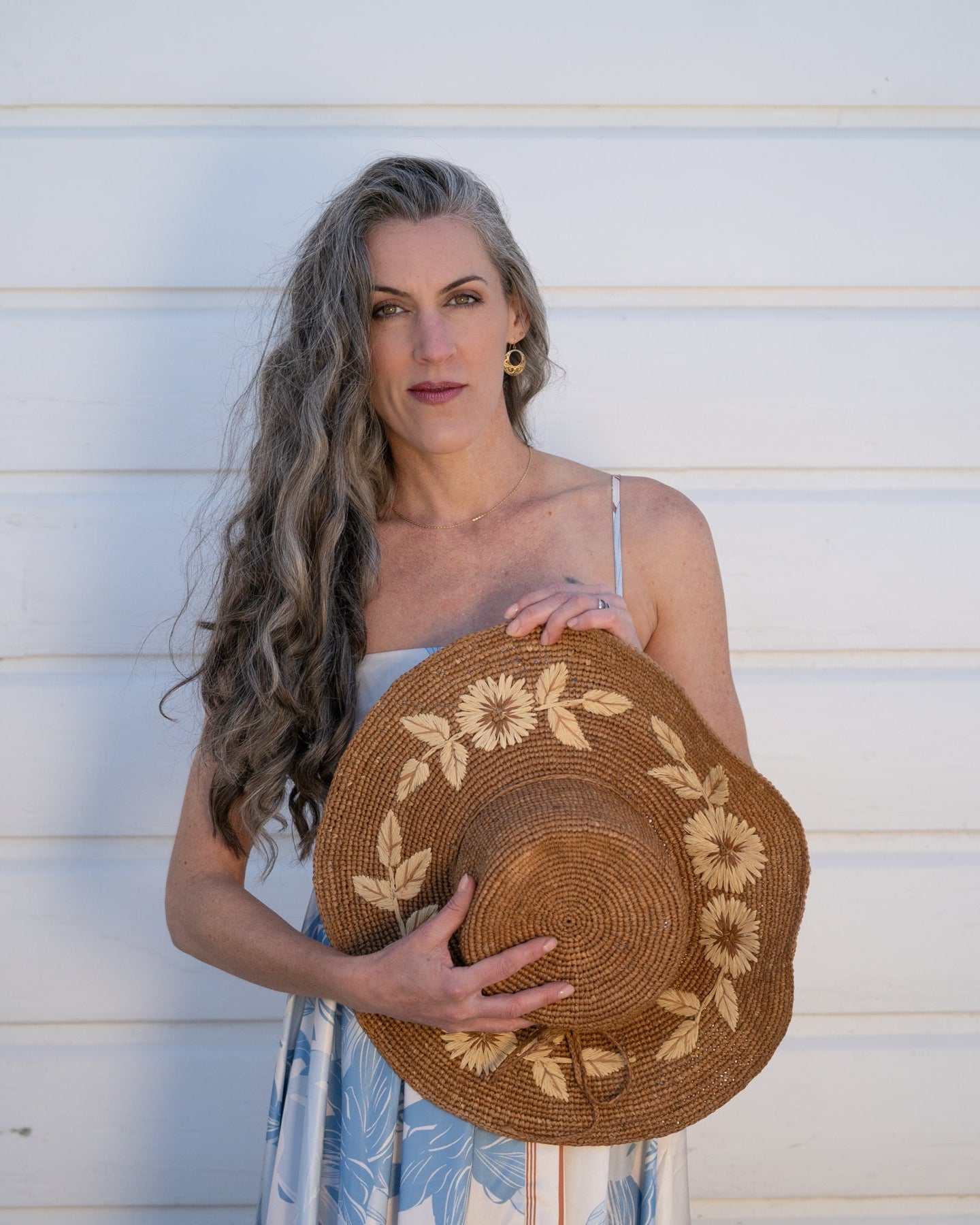 Model wearing 5.5" Brim Gigi Cinnamon and Natural Floral Embroidered Crochet Straw Sun Hats handmade crochet natural raffia palm fiber in a solid hue of cinnamon dark brown making a concentric pattern from the center top of the flattened crown spiraling out to the edge of the brim with matching adjustable raffia braid hat band and natural straw color floral pattern with leaves embroidered on the brim - Shebobo
