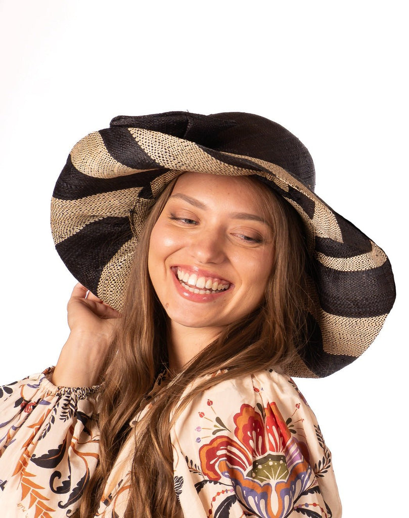 Model wearing 5" Wide Brim Black Two Tone Wide Stripe Straw Sun Hats with Big Bow handmade loomed raffia palm fiber in a solid hue of Black on the crown and matching oversized big bow embellishment hat band, with two tone even width wide stripe pattern of black and natural straw color that creates a swirl patterned brim - Shebobo