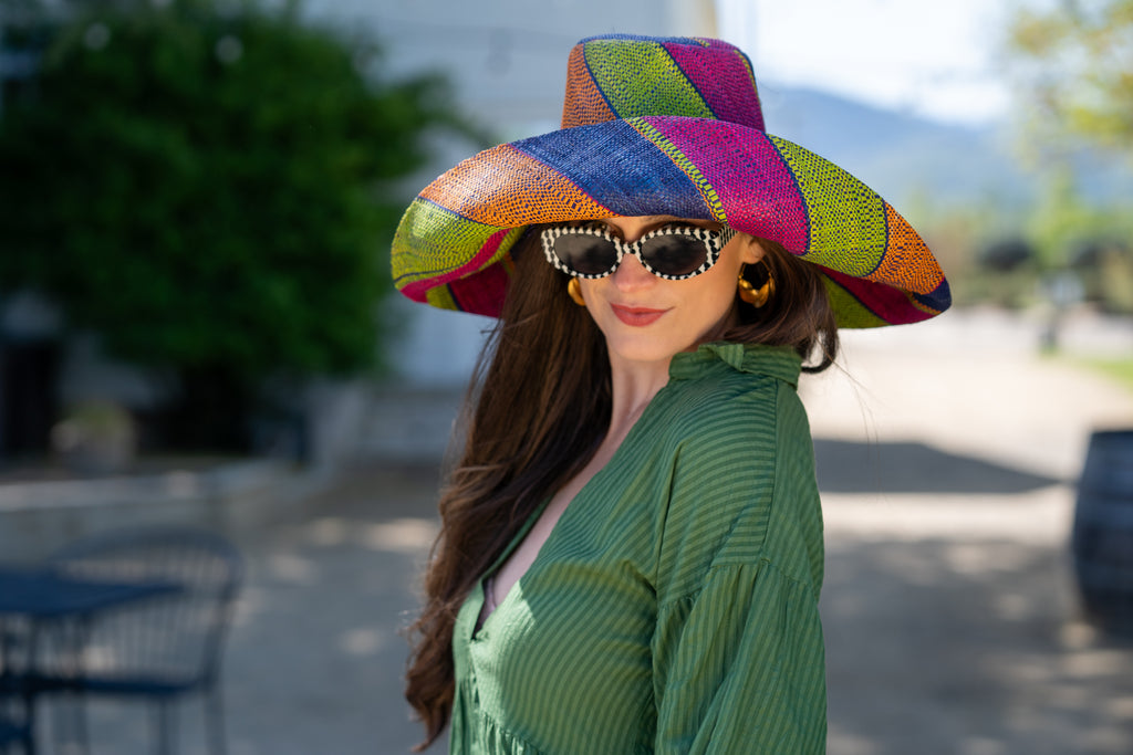 Model wearing 7" Wide Brim Caribbean Swirl Multicolor Stripes Packable Straw Sun Hat Handmade loomed raffia in multi width bands of fuchsia pink, orange, dusk navy/dark/blue, and lime green create a swirl pattern - Shebobo