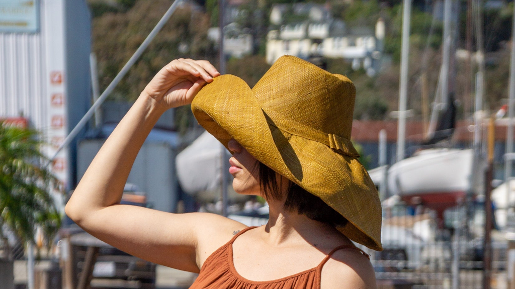 Model wearing 7" Wide Brim Cinnamon Packable Straw Sun Hat handmade loomed natural raffia palm fiber in a solid hue of cinnamon/tobacco/brown - Shebobo