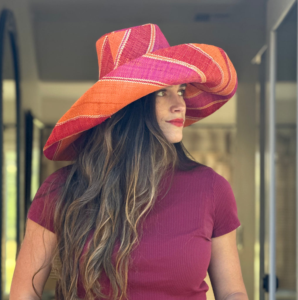 Model wearing 5" & 7" Wide Brim Fuchsia & Coral Swirl Multicolor Stripes Packable Straw Sun Hat Handmade loomed raffia in multi width bands of fuchsia pink, coral orange, red, and natural straw color create a swirl pattern - Shebobo