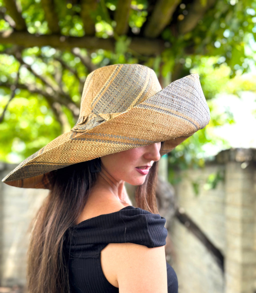 Model wearing 5" & 7" Wide Brim Latte Swirl Multicolor Stripes Packable Straw Sun Hat Handmade loomed raffia in multi width bands of latte/light brown, grey, and natural create a swirl pattern - Shebobo