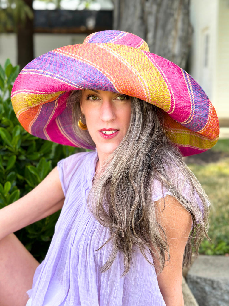 Model wearing 5" & 7" Wide Brim Midori Swirl Multicolor Stripes Packable Straw Sun Hat Handmade loomed raffia in multi width bands of orange, lime green, fuchsia pink, purple, etc. create a swirl pattern - Shebobo