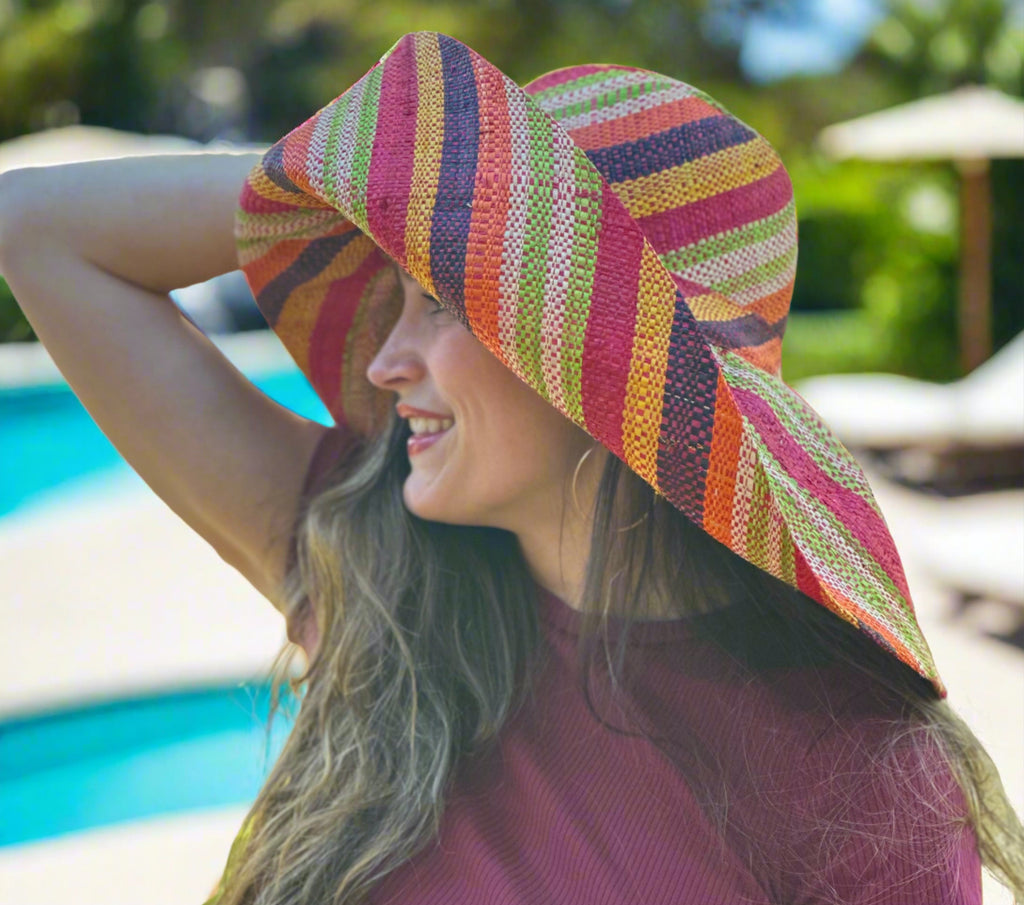 Model wearing 5" & 7" Wide Brim Orange Stripe Multicolor Stripes Packable Straw Sun Hat Handmade loomed raffia multi width bands of orange, yellow, red, black, lime green, and natural straw color create a swirl pattern - Shebobo