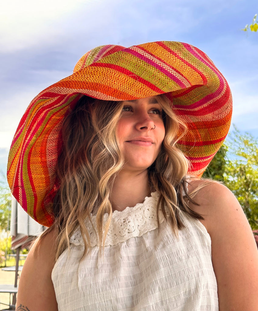 Model wearing 5" & 7" Wide Brim Sunrise Stripe Multicolor Stripes Packable Straw Sun Hat Handmade loomed raffia in multi width bands of saffron yellow, fuchsia pink, orange, red, lime green, and natural create a swirl pattern - Shebobo