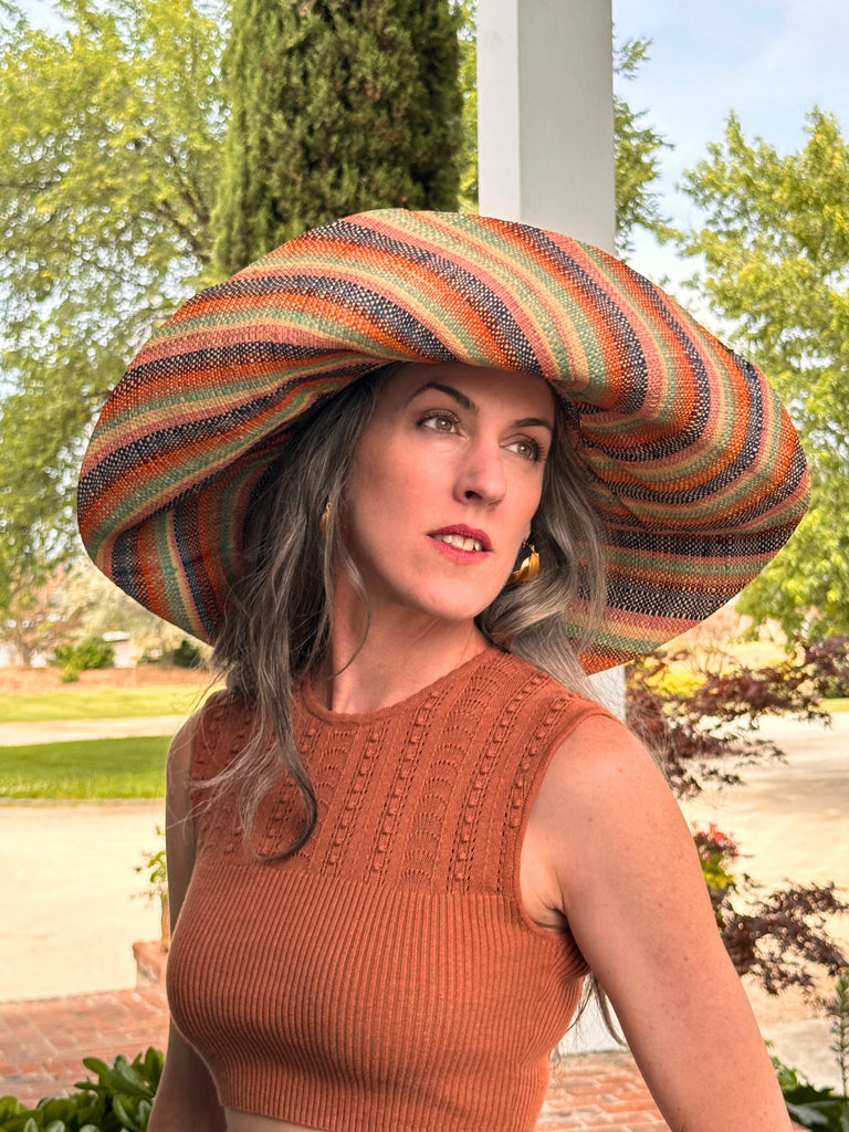 Model wearing 5" & 7" Wide Brim Taffy Multicolor Stripes Packable Straw Sun Hat Handmade loomed raffia in multi width bands of saffron yellow, turquoise blue, seafoam blue/green, orange, pink, bordeaux red, etc., and natural create a swirl pattern - Shebobo