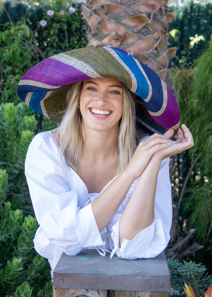 Model wearing 7" Wide Brim Olive and Purple Swirl Multicolor Stripes Packable Straw Sun Hat Handmade loomed raffia multi width bands of turquoise blue, olive green, purple, and natural straw color create a swirl pattern - Shebobo