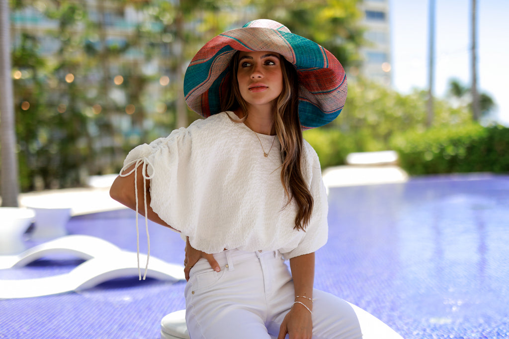 Model wearing 7" Wide Brim Peach & Turquoise Swirl Packable Straw Sun Hat handmade loomed raffia in multi width stripes of turquoise blue, peach, and blush orange/pink create a swirl pattern - Shebobo