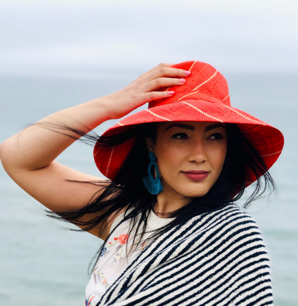 Model wearing 5" Wide Brim Coral Pinstripes Packable Straw Sun Hat handmade loomed raffia in wide stripes of coral red/orange with narrow stripes of natural creating a swirl pattern - Shebobo