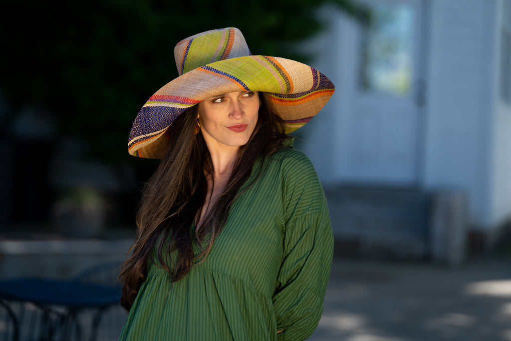Model wearing 7" Wide Brim Rio Swirl Multicolor Stripes Packable Straw Sun Hat Handmade loomed raffia in multi width bands of cappuccino light brown, lime green, saffron yellow, red, purple, navy blue, natural straw color, etc. create a swirl pattern - Shebobo