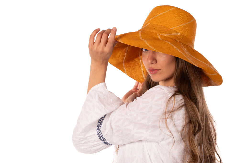 Model wearing 5" Wide Brim Saffron Pinstripes Packable Straw Sun Hat handmade loomed raffia in wide stripes of saffron yellow/orange with narrow stripes of natural creating a swirl pattern - Shebobo