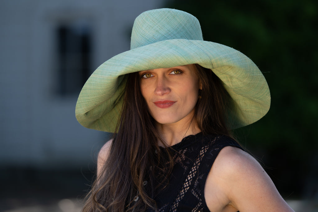 Model wearing 7" Wide Brim Seafoam Packable Straw Sun Hat handmade loomed raffia in a solid hue of seafoam light/green/blue lightweight malleable flexible sun protection hat - Shebobo