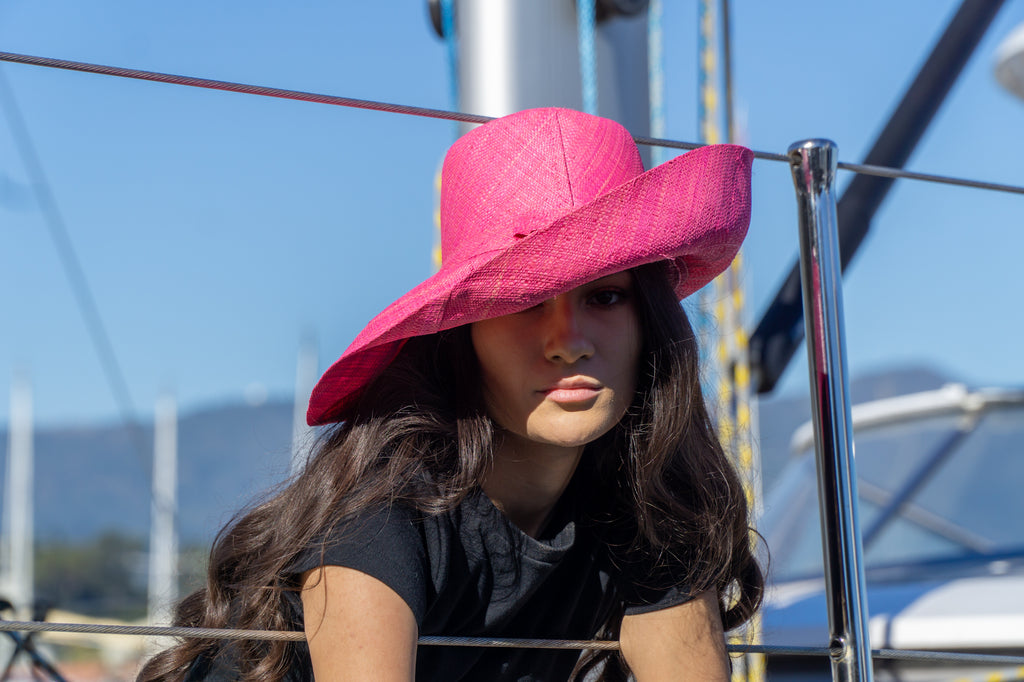 Model wearing 5" Wide Brim Solid Color Packable Straw Sun Hat handmade loomed raffia in a solid hue of fuchsia bright/hot/barbie pink- Shebobo