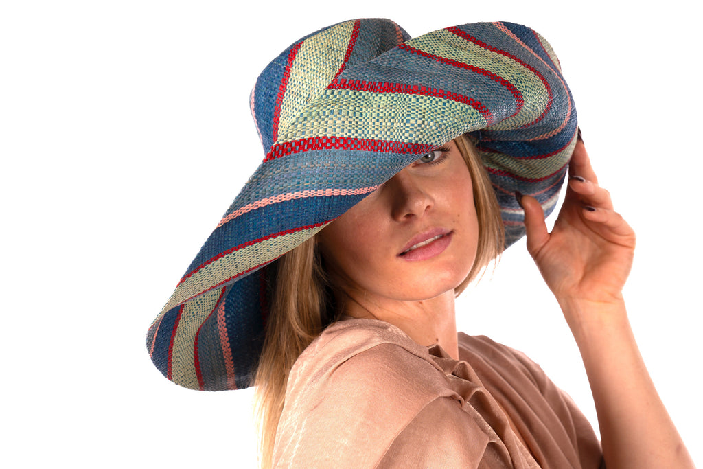 Model wearing 7" Wide Brim Teal Swirl Multicolor Stripes Packable Straw Sun Hat Handmade loomed raffia in multi width bands of teal blue/green, seafoam green/blue, red, and pink create a swirl pattern - Shebobo