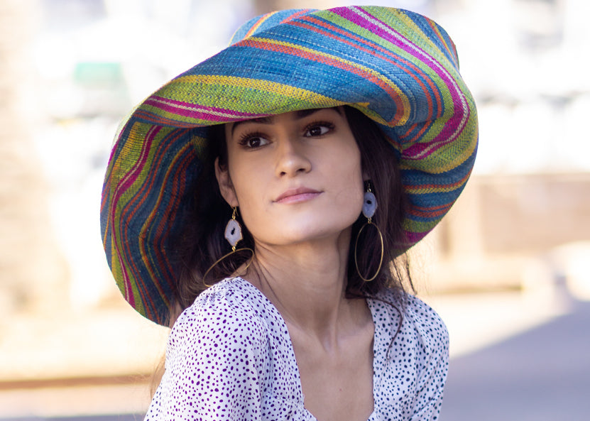 Model wearing  7" Wide Brim Turquoise and Lime Multicolor Stripes Packable Straw Sun Hat Handmade loomed raffia multi width bands of turquoise blue, lime green, fuchsia pink, orange, yellow, and natural straw color create a swirl pattern - Shebobo