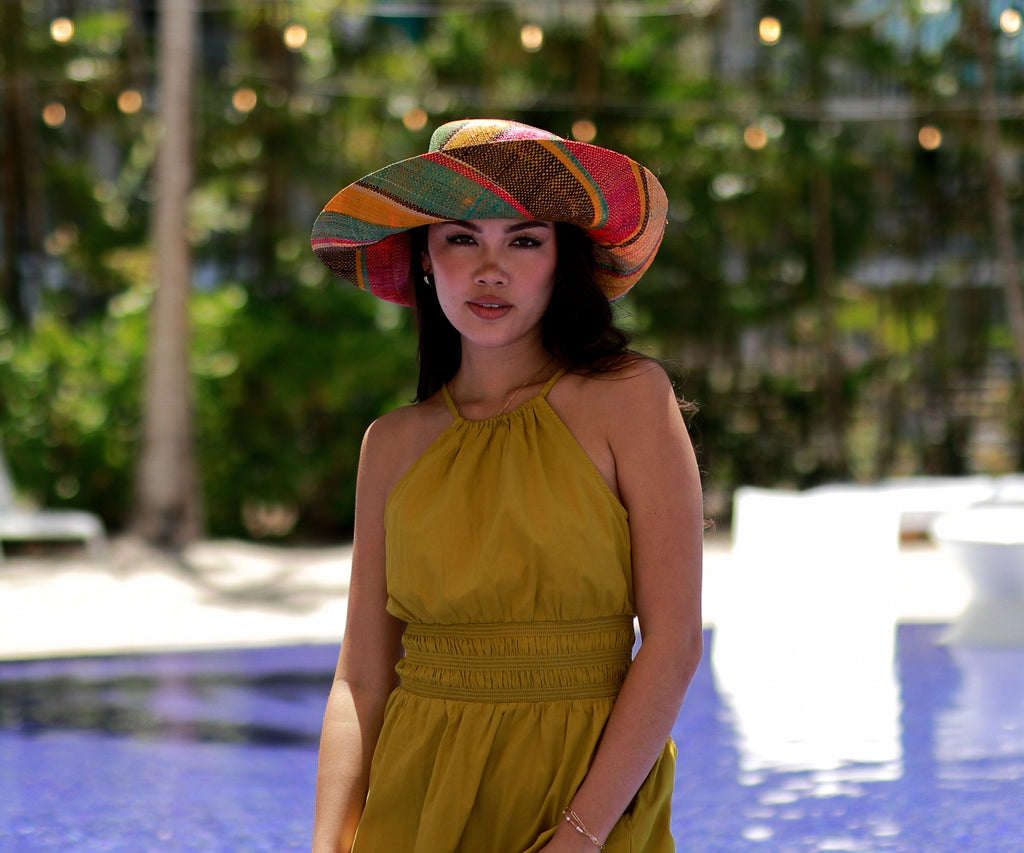 Model wearing 5" Brim Carmalita Multicolor Stripes Packable Straw Sun Hat Handmade loomed raffia in multi width bands of saffron yellow, fuchsia pink, turquoise blue, black, and natural create a swirl pattern - Shebobo