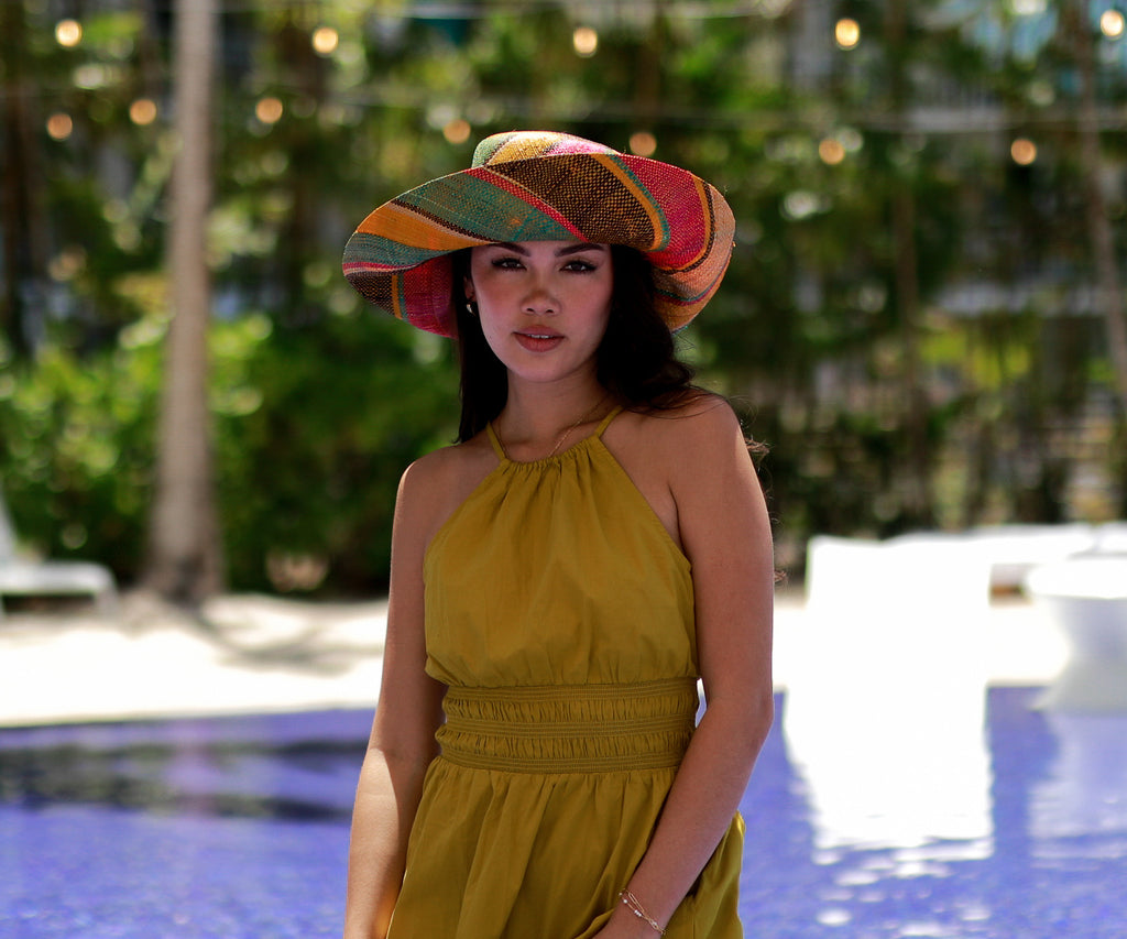 Model wearing 5 inch wide brim Carmalita Multicolor Stripe Straw Sun Hat handmade loomed raffia palm fiber in multi width bands of saffron yellow, fuchsia pink, seafoam turquoise/blue/green, black, and natural straw color that create a swirl pattern lightweight, packable, moldable, uv protection sun hat - Shebobo