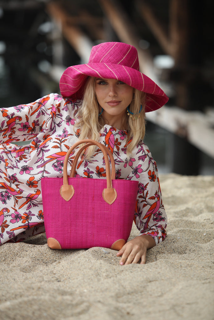 Model wearing 5" Wide Brim Fuchsia Pinstripes Packable Straw Sun Hat handmade loomed raffia in fuchsia pink wide stripes with narrow natural colored pinstripes running through create a swirl pattern - Shebobo (with Augustine Fuchsia Small Straw Basket Bag)