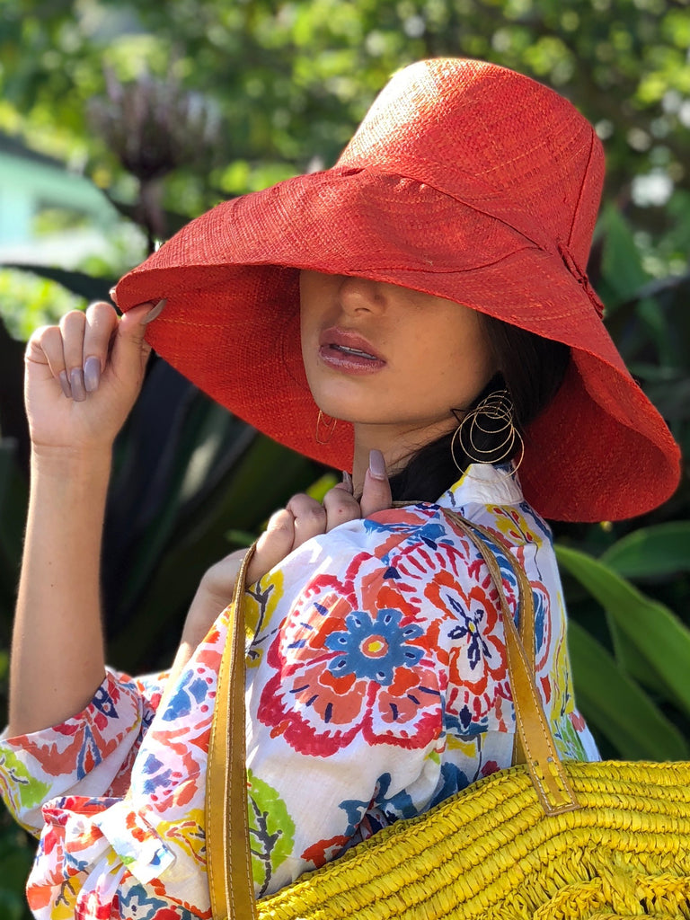 Model wearing 5"  Wide Brim Solid Color Packable Straw Sun Hat handmade loomed raffia in a solid hue of coral orange/red - Shebobo