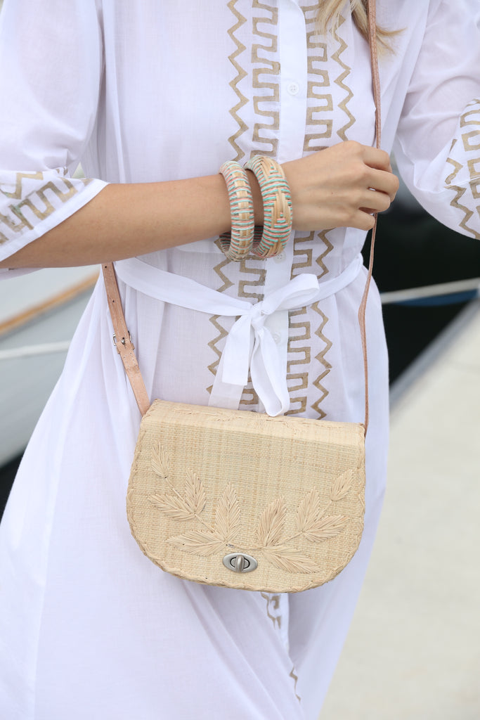 Model wearing 70's Crossbody Straw Bag handmade loomed natural raffia palm fiber purse with natural colored accent cross stitch edging and matching leaf design embroidery handbag with adjustable leather strap - Shebobo