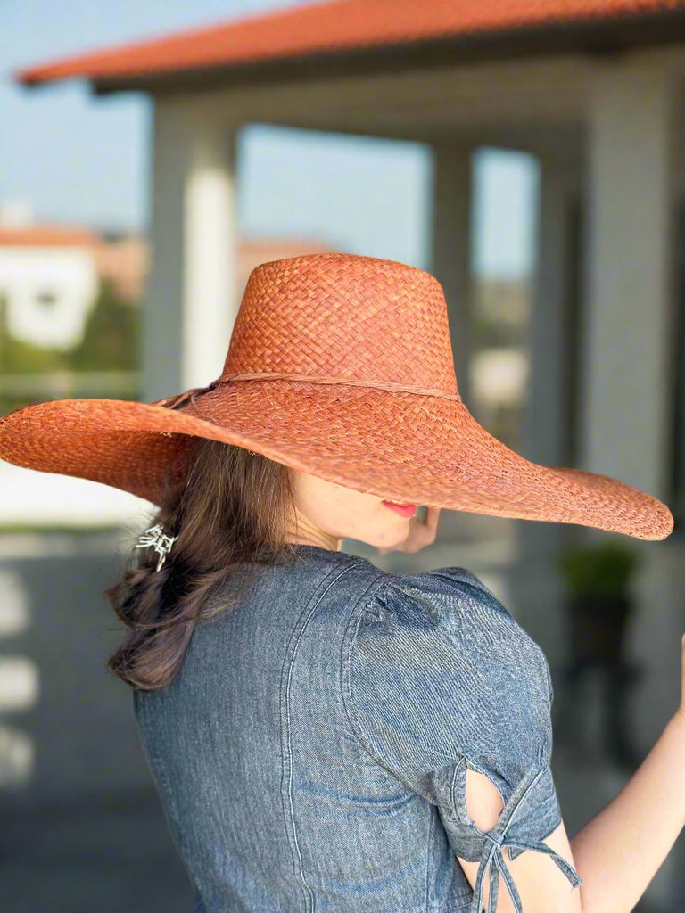 Model wearing 7" Brim Natasha Whisky Woven XL Straw Sun Hat handmade woven natural raffia palm fiber in a solid hue of whisky red/brown with matching adjustable twisted raffia hat band and and extra wide brim - Shebobo