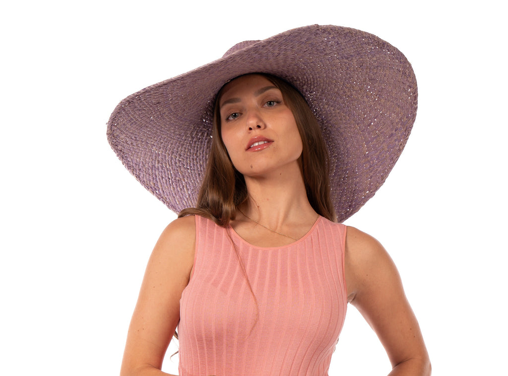 Model wearing 7" Brim Natasha Wisteria Woven XL Straw Sun Hat handmade woven natural raffia palm fiber in a solid hue of wisteria/lavender/lilac pink/purple with matching adjustable twisted raffia hat band and and extra wide brim - Shebobo