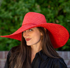 Model wearing 7" Wide Brim Natasha Red Woven XL Straw Sun Hat handmade woven natural raffia palm fiber in a solid hue of red with matching adjustable twisted raffia hat band and and extra wide brim - Shebobo