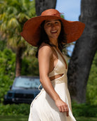 Model wearing 7" Wide Brim Natasha Caramel Woven XL Straw Sun Hat handmade woven natural raffia palm fiber in a solid hue of whisky red/brown with matching adjustable twisted raffia hat band and and extra wide brim - Shebobo