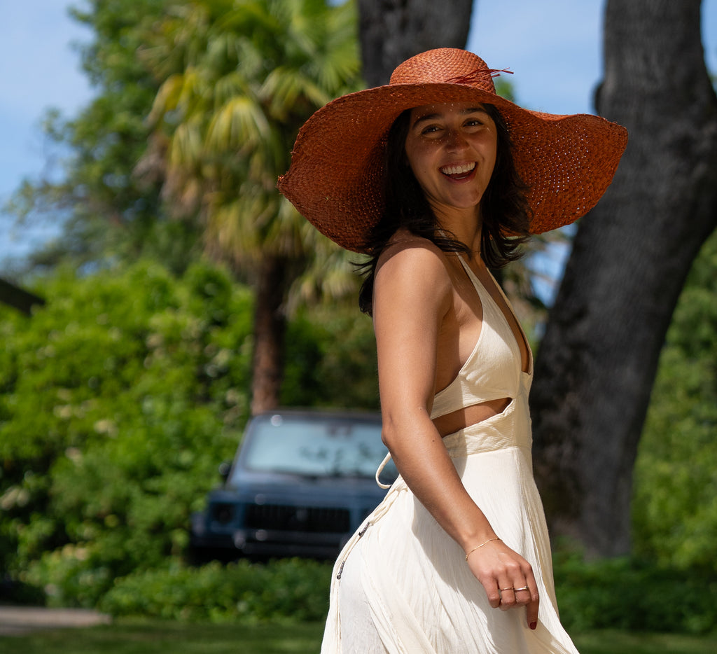 Model wearing 7" Wide Brim Natasha Caramel Woven XL Straw Sun Hat handmade woven natural raffia palm fiber in a solid hue of whisky red/brown with matching adjustable twisted raffia hat band and and extra wide brim - Shebobo