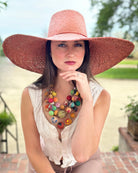Model wearing 7" Wide Brim Natasha Rouge Woven XL Straw Sun Hat handmade woven natural raffia palm fiber in a solid hue of rouge red/pink with matching adjustable twisted raffia hat band and and extra wide brim - Shebobo