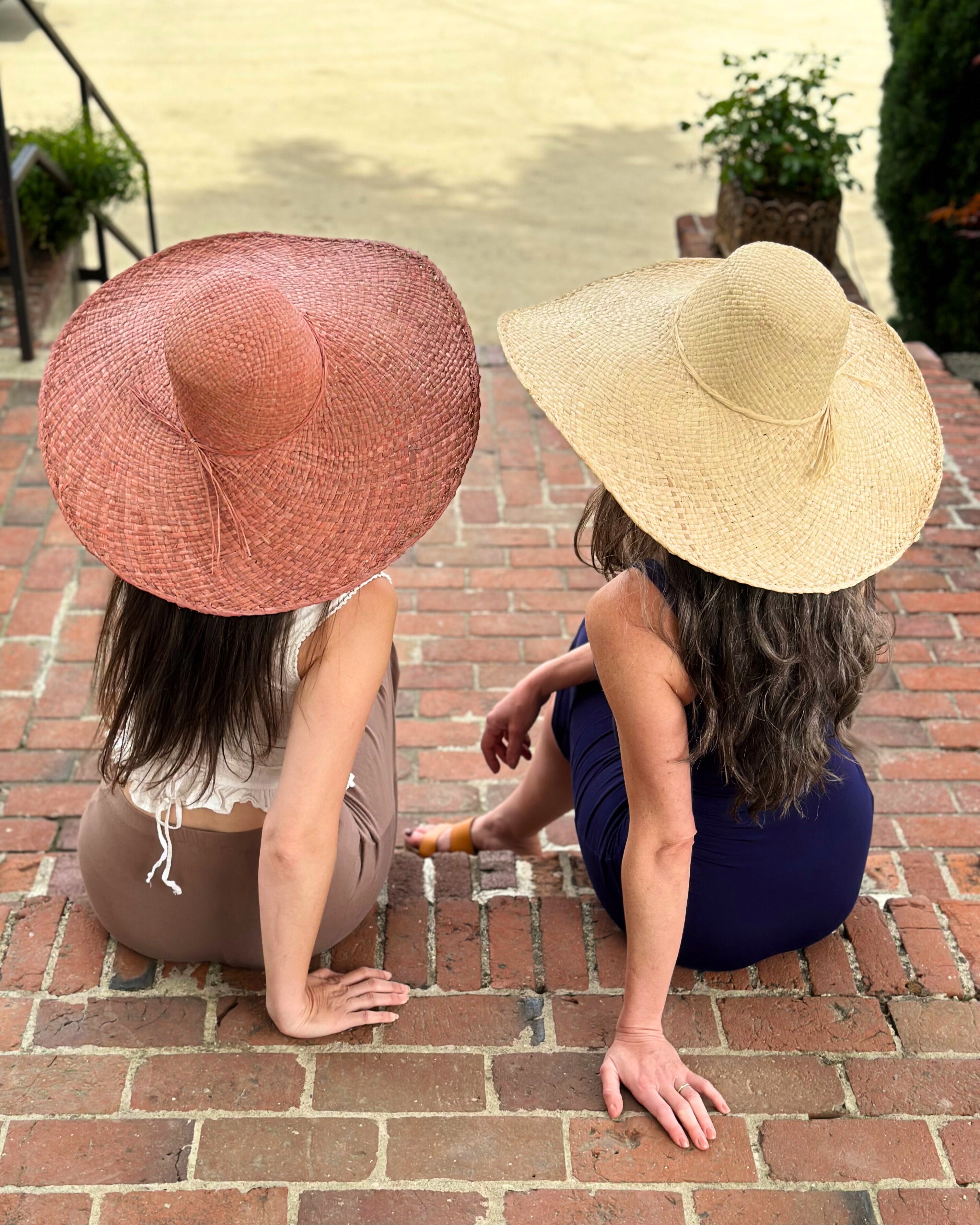 Model wearing 7" Wide Brim Natasha Natural Woven XL Straw Sun Hat handmade woven natural raffia palm fiber in a solid hue of straw color with matching adjustable twisted raffia hat band and and extra wide brim and the same hat in Rouge pink/red hue - Shebobo