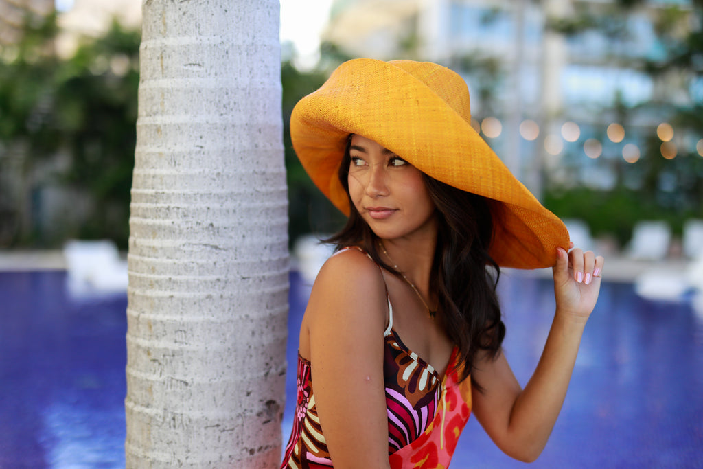 Model wearing 7" Wide Brim Solid Color Packable Straw Sun Hat handmade loomed raffia in a solid hue of saffron yellow - Shebobo