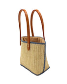 Side view Adele Mini Crochet Raffia Straw Handbag Purse with Colored Edge Natural & Denim handmade crochet raffia palm fiber in a solid hue of natural straw color with contrasting narrow band of denim light/blue around the outer edges of the bag with subtle vertical band texture and leather handles - Shebobo