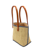 Side view Adele Mini Crochet Raffia Straw Handbag Purse with Colored Edge Natural & Denim handmade crochet raffia palm fiber in a solid hue of natural straw color with contrasting narrow band of denim light/blue around the outer edges of the bag with subtle vertical band texture and leather handles - Shebobo
