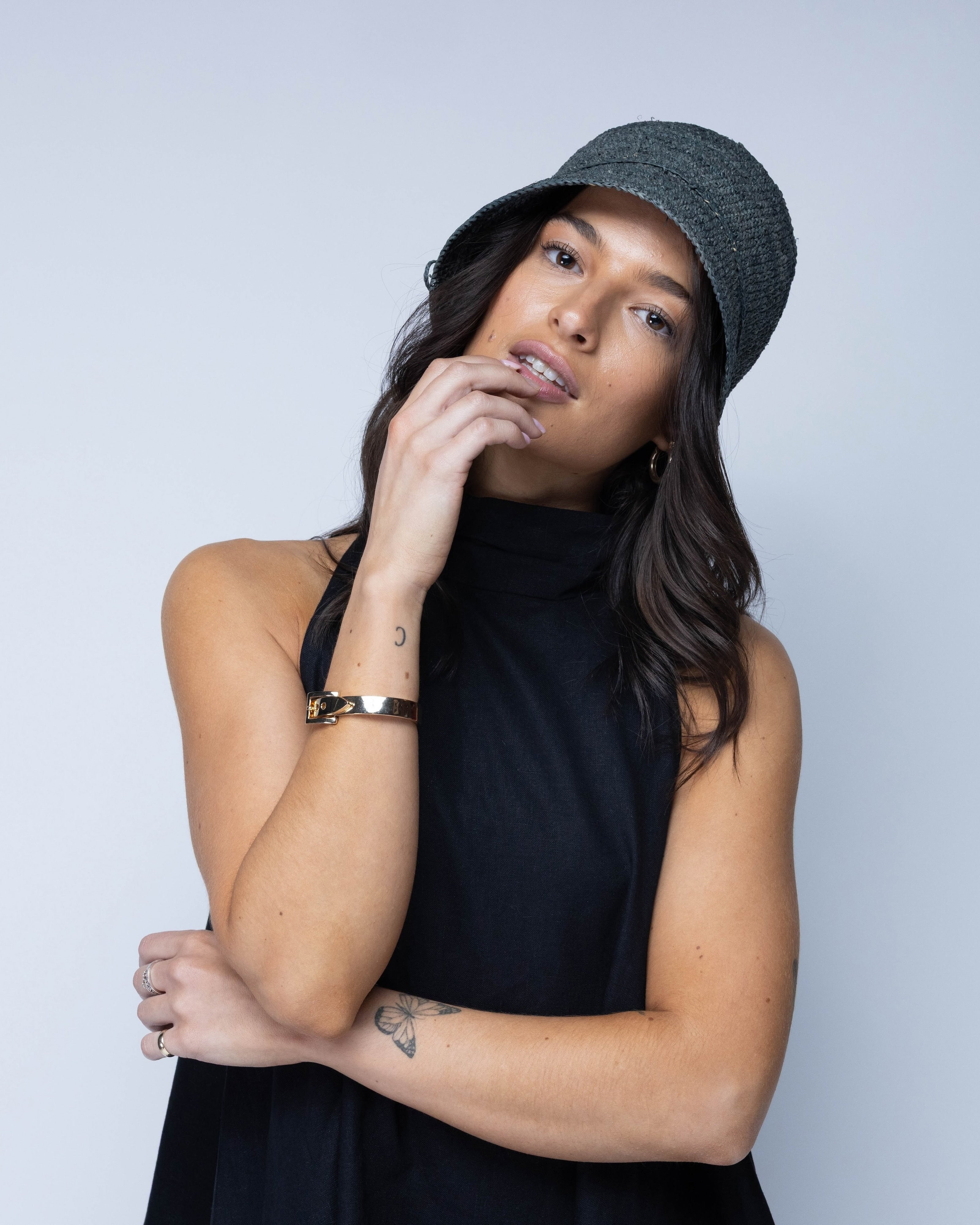 Model wearing Ali 2" Brim Crochet Bucket Raffia Straw Hats handmade natural raffia palm fiber in a subtle crochet link texture spiraling out from the top crown of the hat to the edge of the brim in a solid hue of gray with matching braided adjustable hat band sun hat - Shebobo