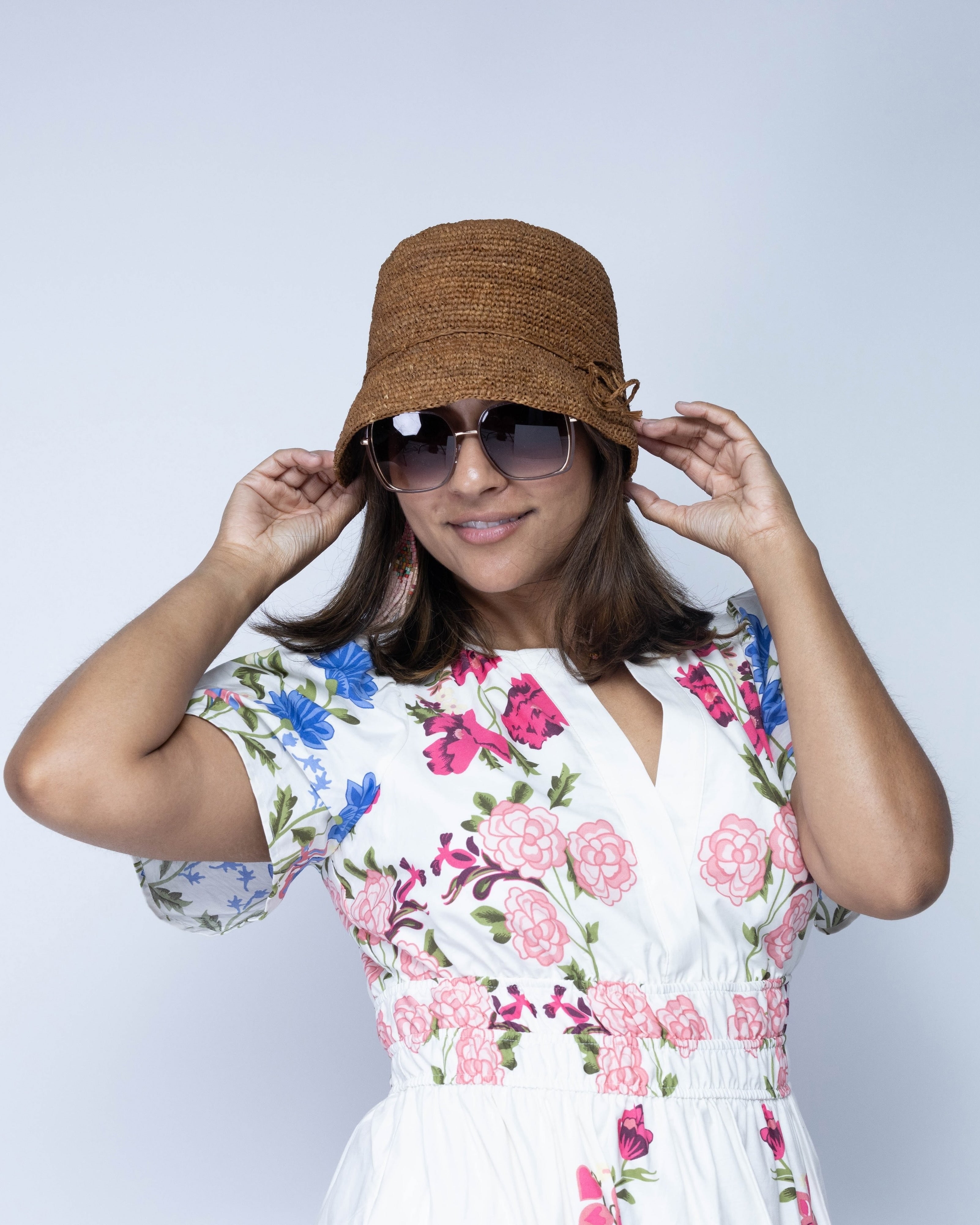 Model wearing Ali 2" Brim Crochet Bucket Raffia Straw Hats handmade natural raffia palm fiber in a subtle crochet link texture spiraling out from the top crown of the hat to the edge of the brim in a solid hue of tobacco cinnamon/dark/brown with matching braided adjustable hat band sun hat - Shebobo