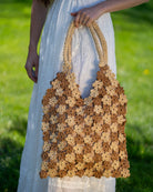 Model wearing Amalie Two Tone Daisy Flower Crochet Straw Handbag handmade crochet mini flower buds from crochet natural raffia palm fiber in an alternating colored pattern of cappuccino tea/light/brown and natural straw color with brown internal liner and natural woven handles purse - Shebobo
