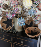 Home decor lifestyle view Amara Raffia Straw Decor Display Basket Bowls: Set of 3 handmade woven natural raffia palm fiber in a crochet loop technique concentric coiled circular pattern with centered black star or flower in the bottom of the bowl that goes up the cinnamon/tobacco/brown sides with matching black flower/arrow pattern on sides set of small, medium, and large straw display bowls - Shebobo