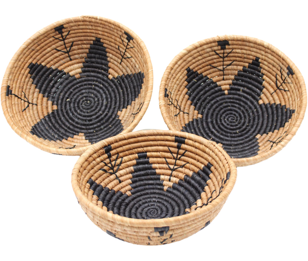 Side view Amara Raffia Straw Decor Display Basket Bowls: Set of 3 handmade woven natural raffia palm fiber in a crochet loop technique concentric coiled circular pattern with centered black star or flower in the bottom of the bowl that goes up the cinnamon/tobacco/brown sides with matching black flower/arrow pattern on sides set of small, medium, and large straw display bowls - Shebobo