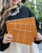 Model wearing Amelia Set of 3 Saffron Nesting Zippered Straw Clutches Pinstripe Pattern handmade loomed raffia in wide vertical bands of saffron yellow with narrow bands of natural straw color with matching zipper and braided zipper pull with cross stitch edging in three sizes of small, medium, and large - Shebobo