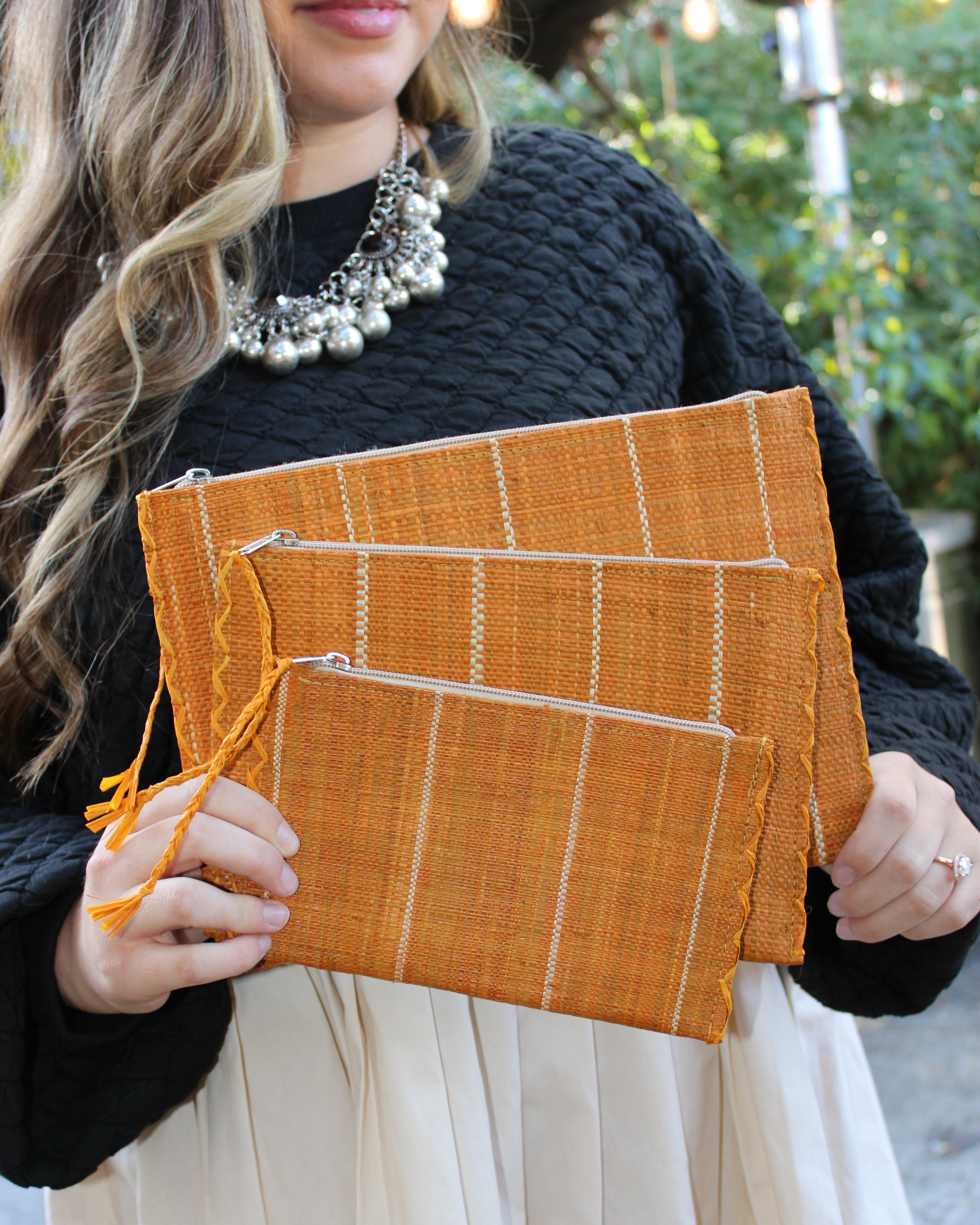 Model wearing Amelia Set of 3 Saffron Nesting Zippered Straw Clutches Pinstripe Pattern handmade loomed raffia in wide vertical bands of saffron yellow with narrow bands of natural straw color with matching zipper and braided zipper pull with cross stitch edging in three sizes of small, medium, and large - Shebobo