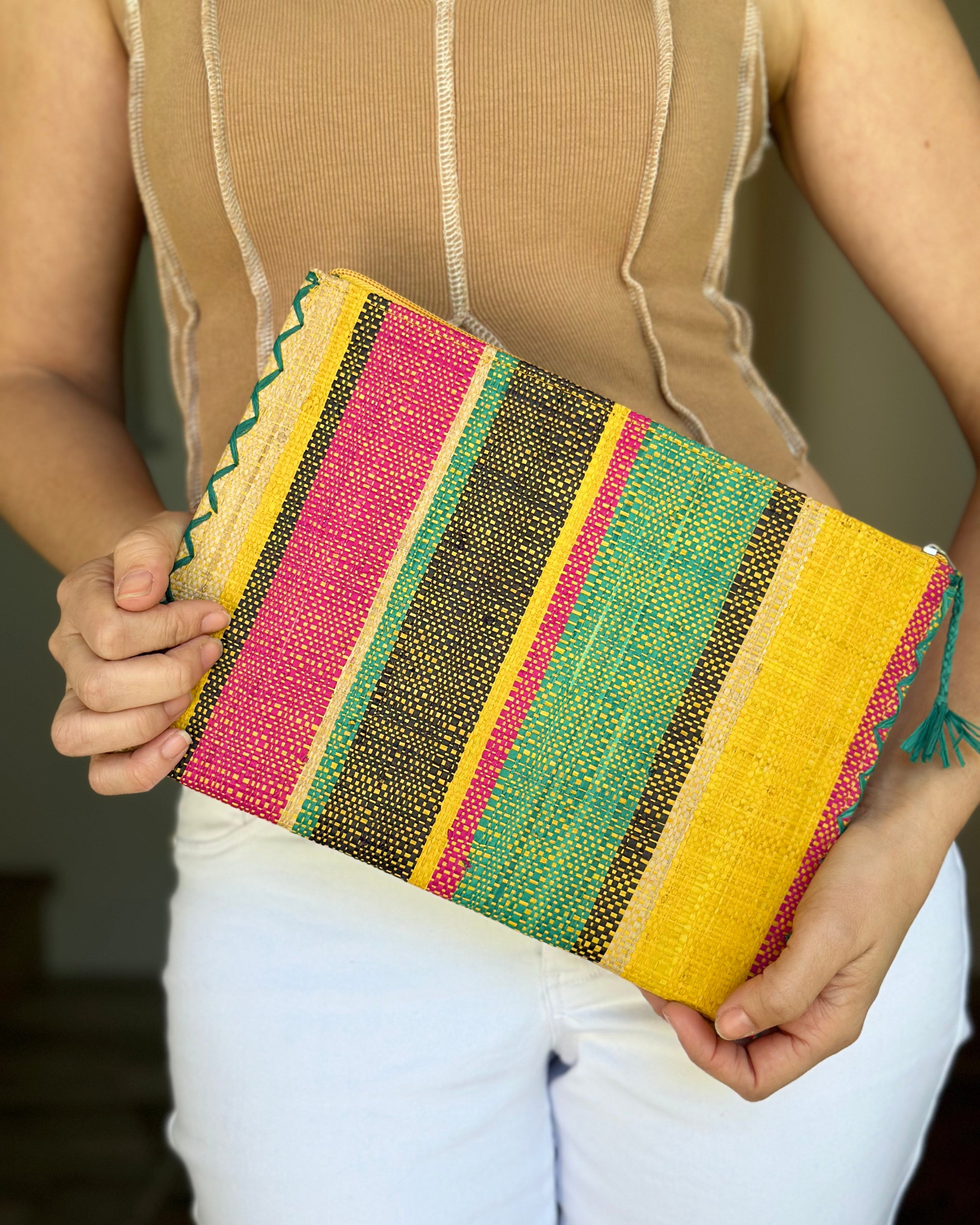 Model wearing Amelia Set of 3 Nesting Zippered Straw Clutches Carmalita Multicolor Stripe Pattern handmade loomed raffia in multiple widths of vertical stripes in turquoise, black, fuchsia, and saffron with matching zipper and braided zipper pull with cross stitch edging in three sizes of small, medium, and large - Shebobo