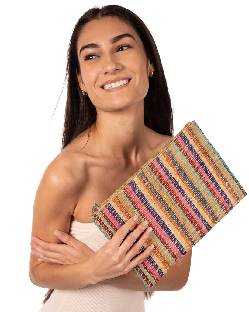 Model wearing Amelia Set of 3 Nesting Zippered Straw Clutches Taffy Multicolor Stripe Pattern handmade loomed raffia in multiple widths of vertical stripes in natural, orange, turquoise, saffron, seafoam, bordeaux, pink with matching zipper and braided zipper pull with cross stitch edging in three sizes of small, medium, and large - Shebobo