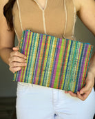 Model wearing Amelia Set of 3 Nesting Zippered Straw Clutches Turquoise Stripe Multicolor Stripe Pattern handmade loomed raffia in multiple widths of vertical stripes in natural, orange, turquoise, saffron, seafoam, red, fuchsia pink, etc. with matching turquoise zipper and braided zipper pull with cross stitch edging in three sizes of small, medium, and large - Shebobo